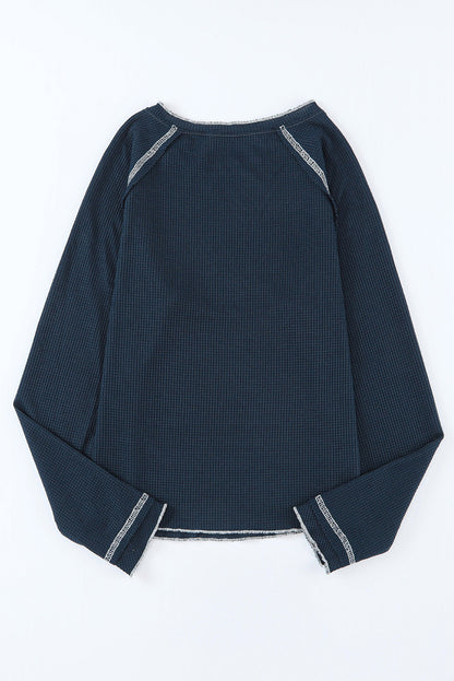 Close-up of navy knit texture and contrast white stitching on open hem sweater.